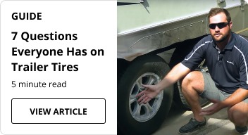 A person kneeling next to a trailer tire.